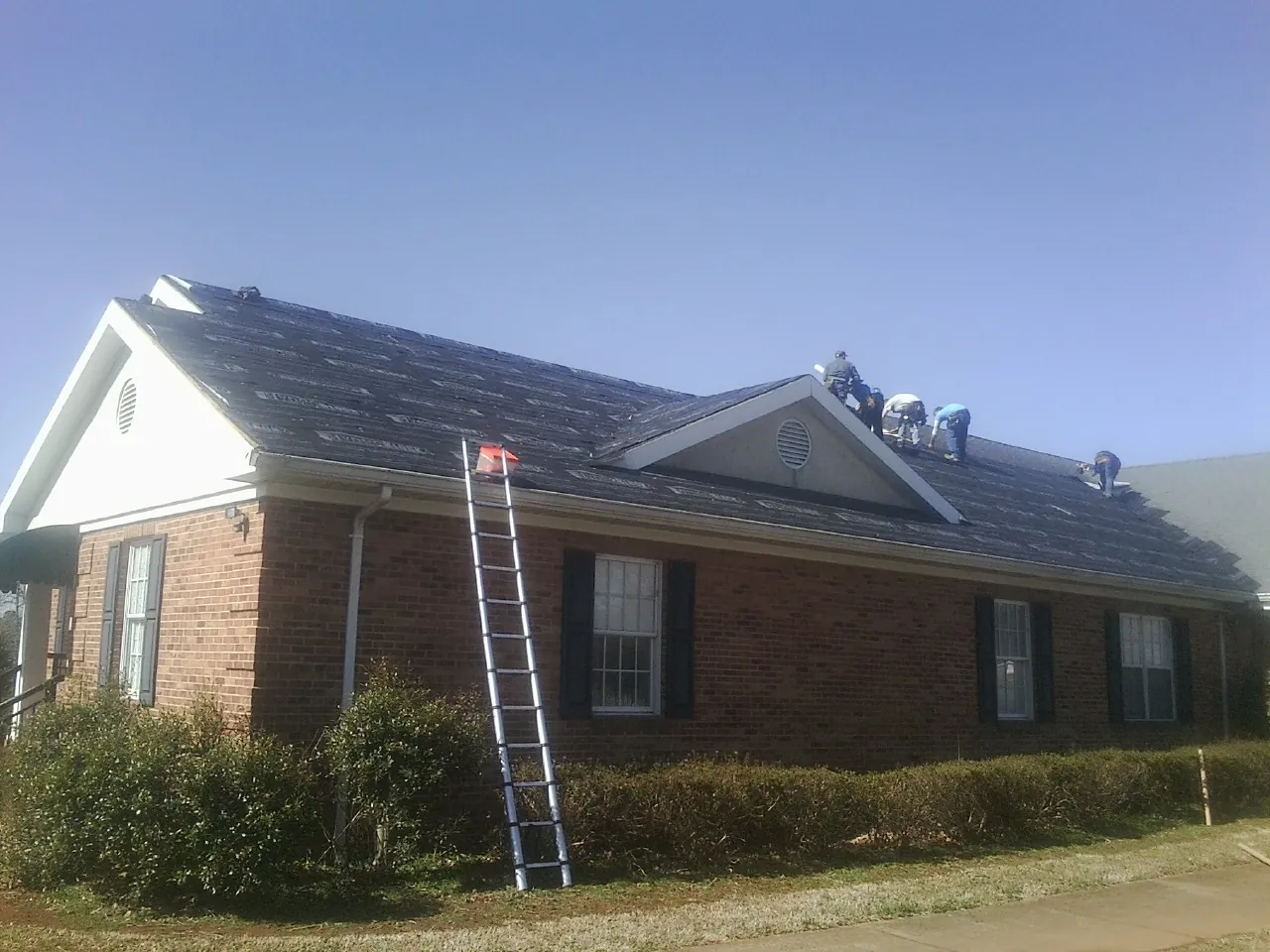 Crew tearing shingles off a brick ranch roof with a ladder set — Emergency Roof Repair work by our crew in Corbett