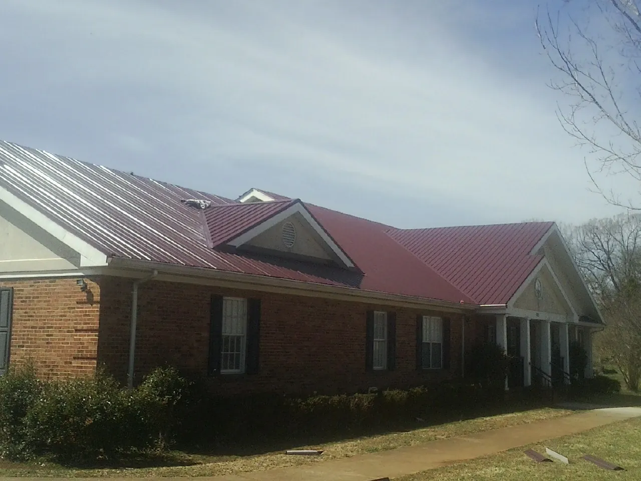 Red metal roof with gabled entries on a long brick building, from a Hail Damage Roof Repair job in Corbett