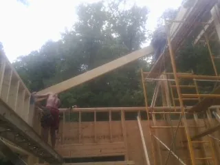 Carpenter raising a rafter beam on a new second story frame in Corbett