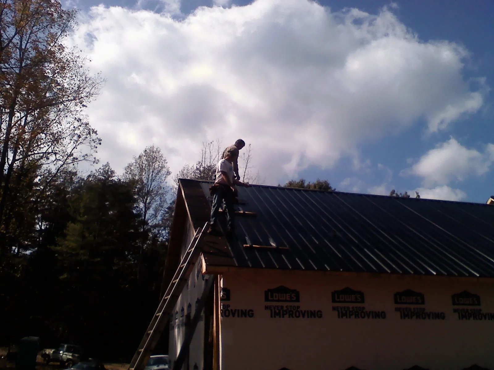 Roofer fastening dark metal panels high against a cloudy sky, from a Roof Inspection job in Corbett